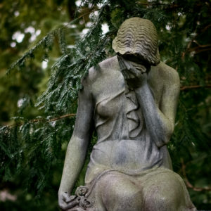 Old marble statue of woman weeping intohand, foliage touching her shoulder 